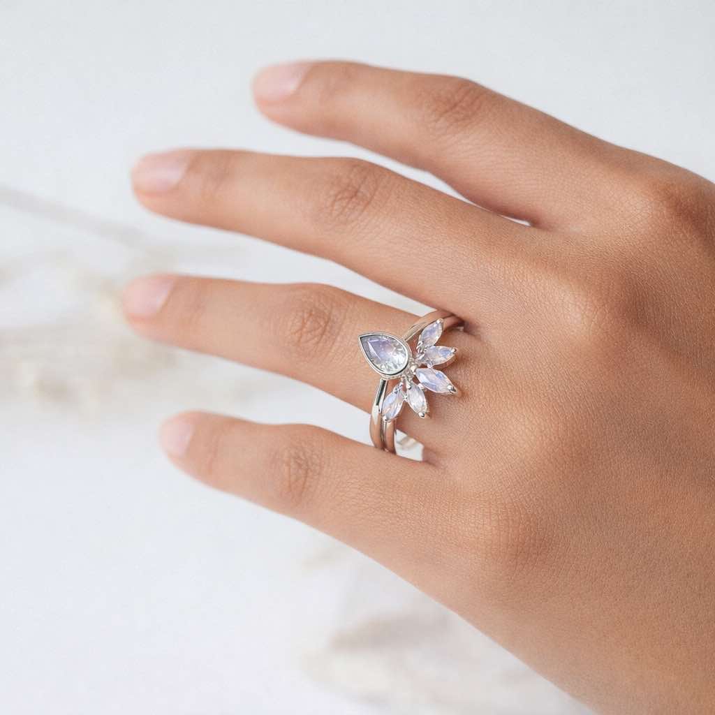 Hand wearing silver rings with a teardrop-shaped moonstones gemstone on a light background