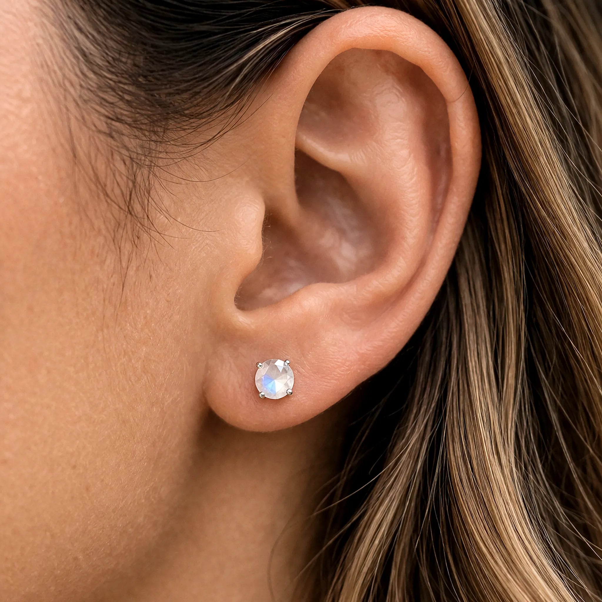 Close-up of an ear wearing a sterling silver stud earring with a natural rainbow moonstone gemstone.
