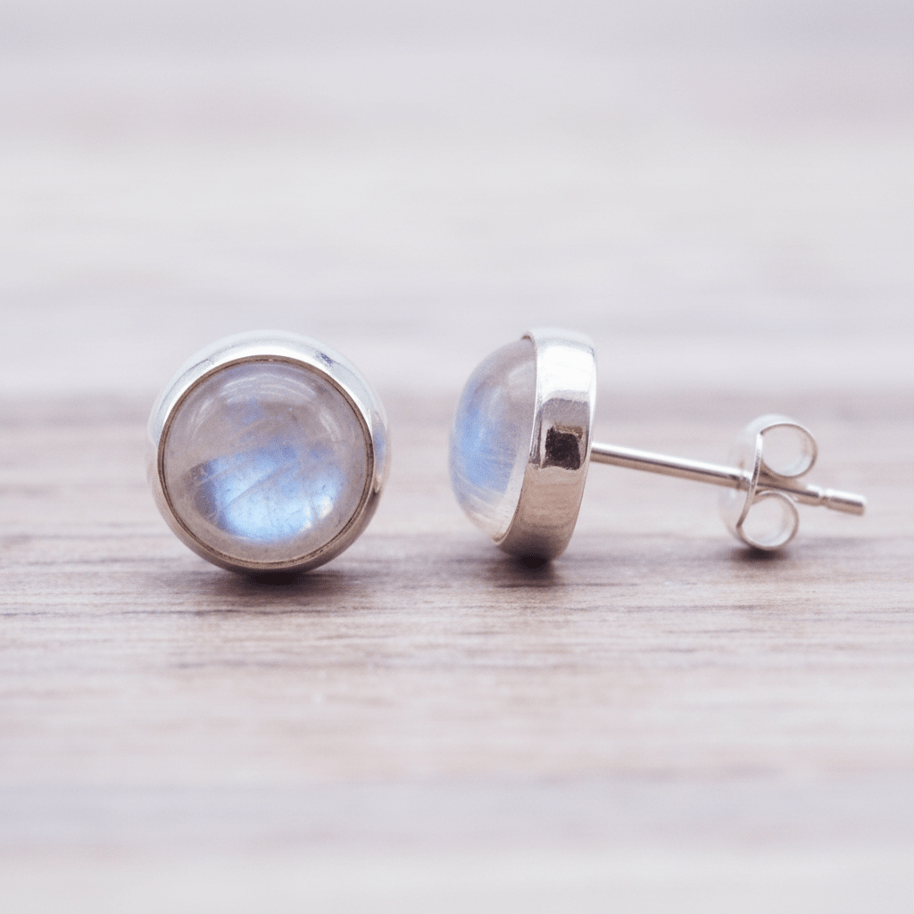 Pair of silver stud earrings with rainbow moonstone gemstones on a light wooden surface