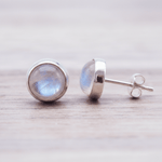 Pair of silver stud earrings with rainbow moonstone gemstones on a light wooden surface