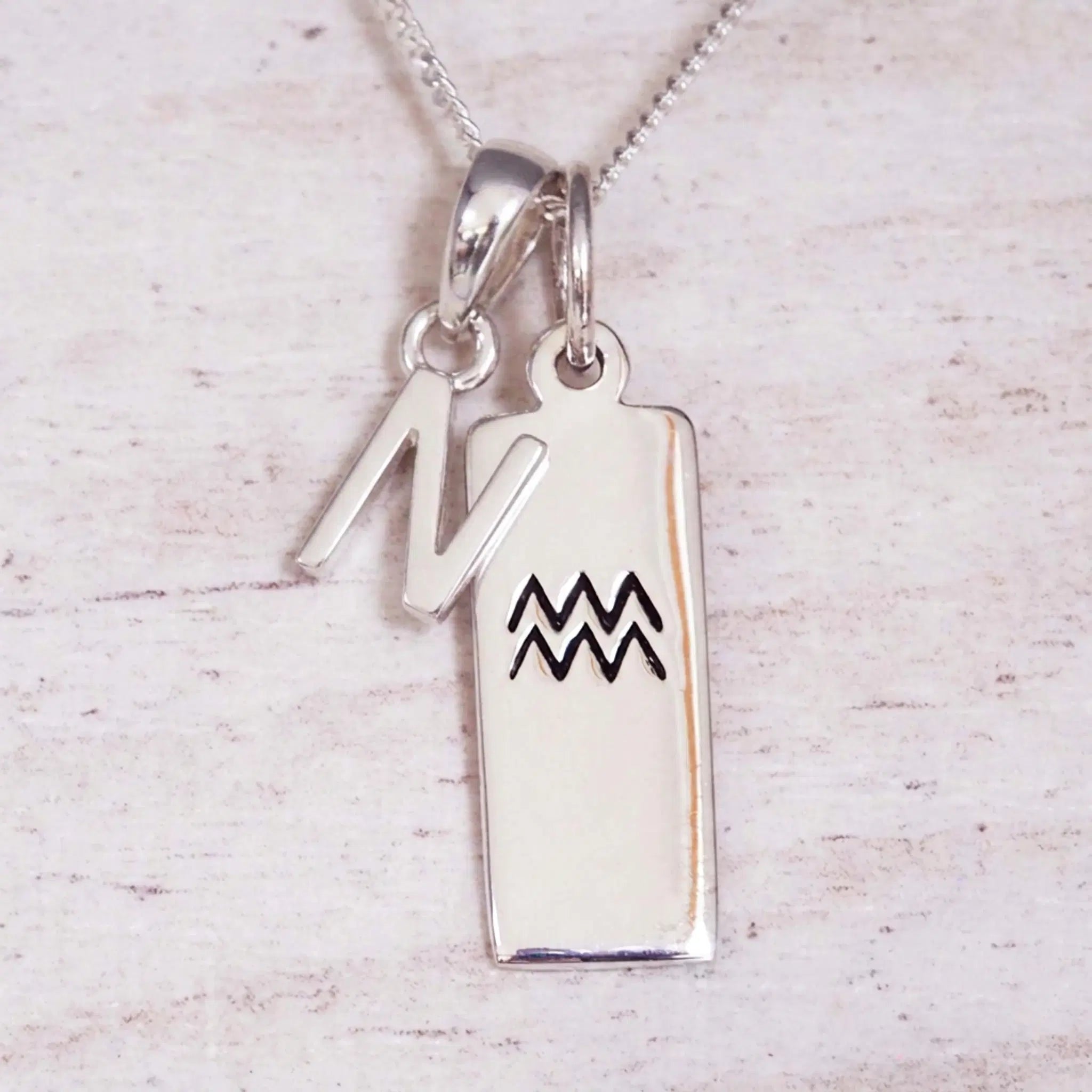Sterling Silver N Initial and Aquarius Necklace on a fine silver chain against a light wooden background