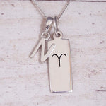 Sterling Silver N Initial pendant and Aries necklace on a fine silver chain on a light wooden background