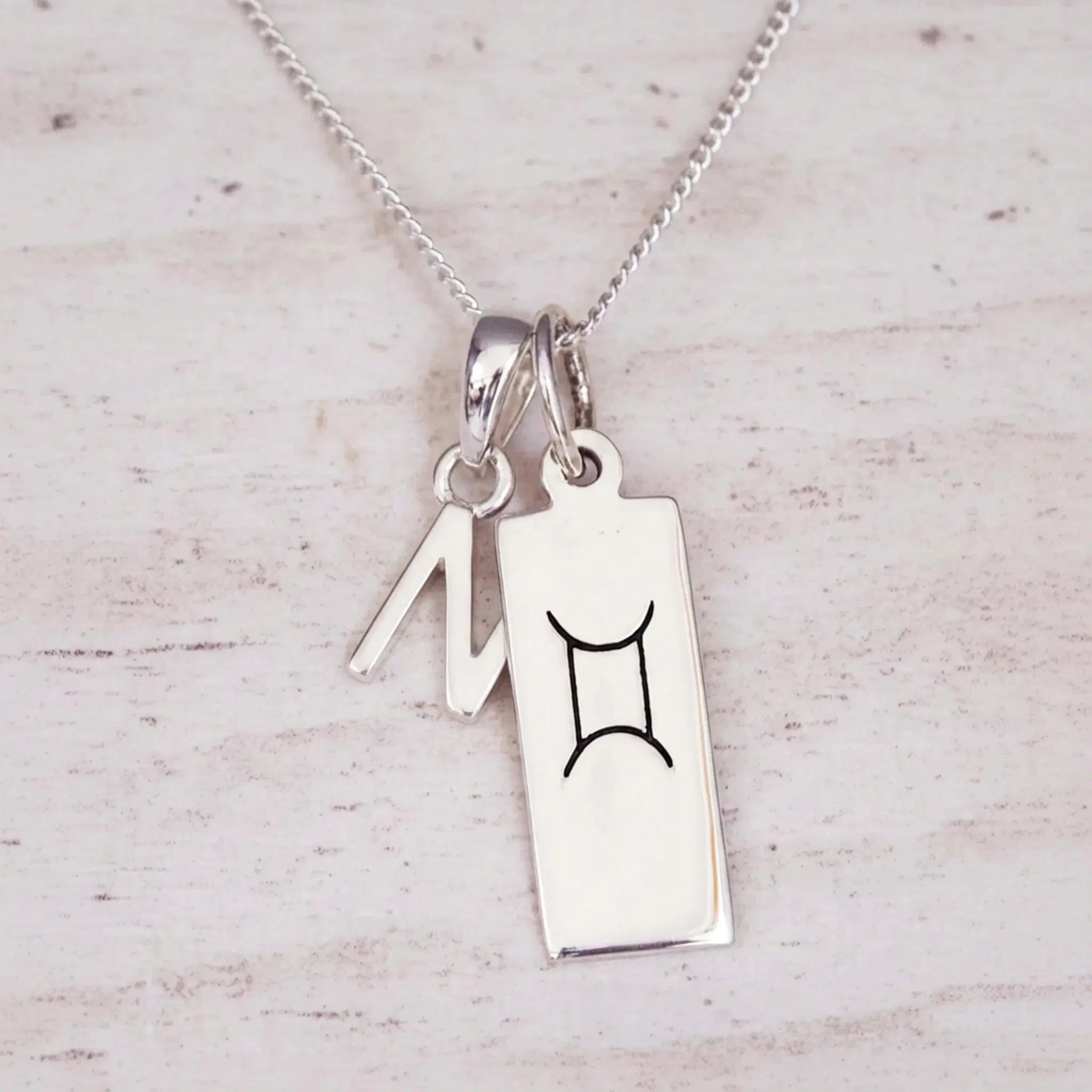 Sterling silver N initial and GeminI Necklace on a fine silver chain on a light wooden background