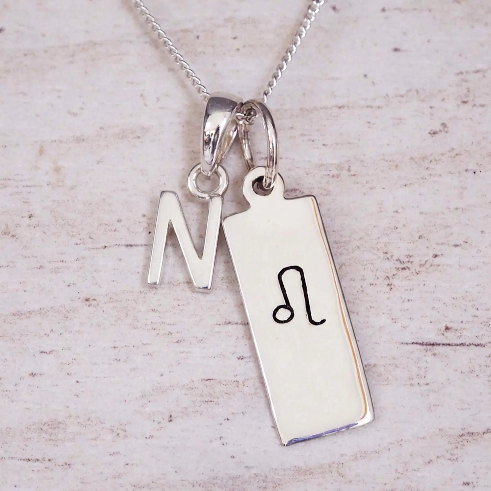 sterling silver initial n leo zodiac star sign pendant necklace against a light wooden background