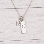 sterling silver N initial Pisces Necklace on a fine silver chain against a light wooden background