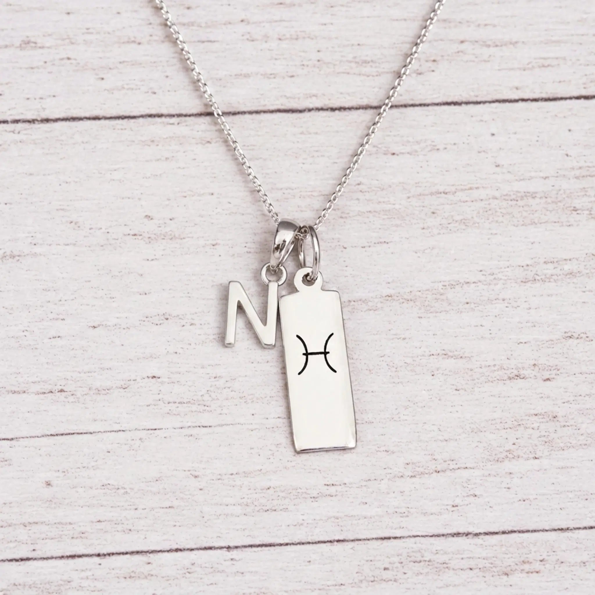 sterling silver N initial Pisces Necklace on a fine silver chain against a light wooden background