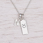 Sterling silver N initial Pendant and Taurus Necklace on a fine silver chain on a light wooden background