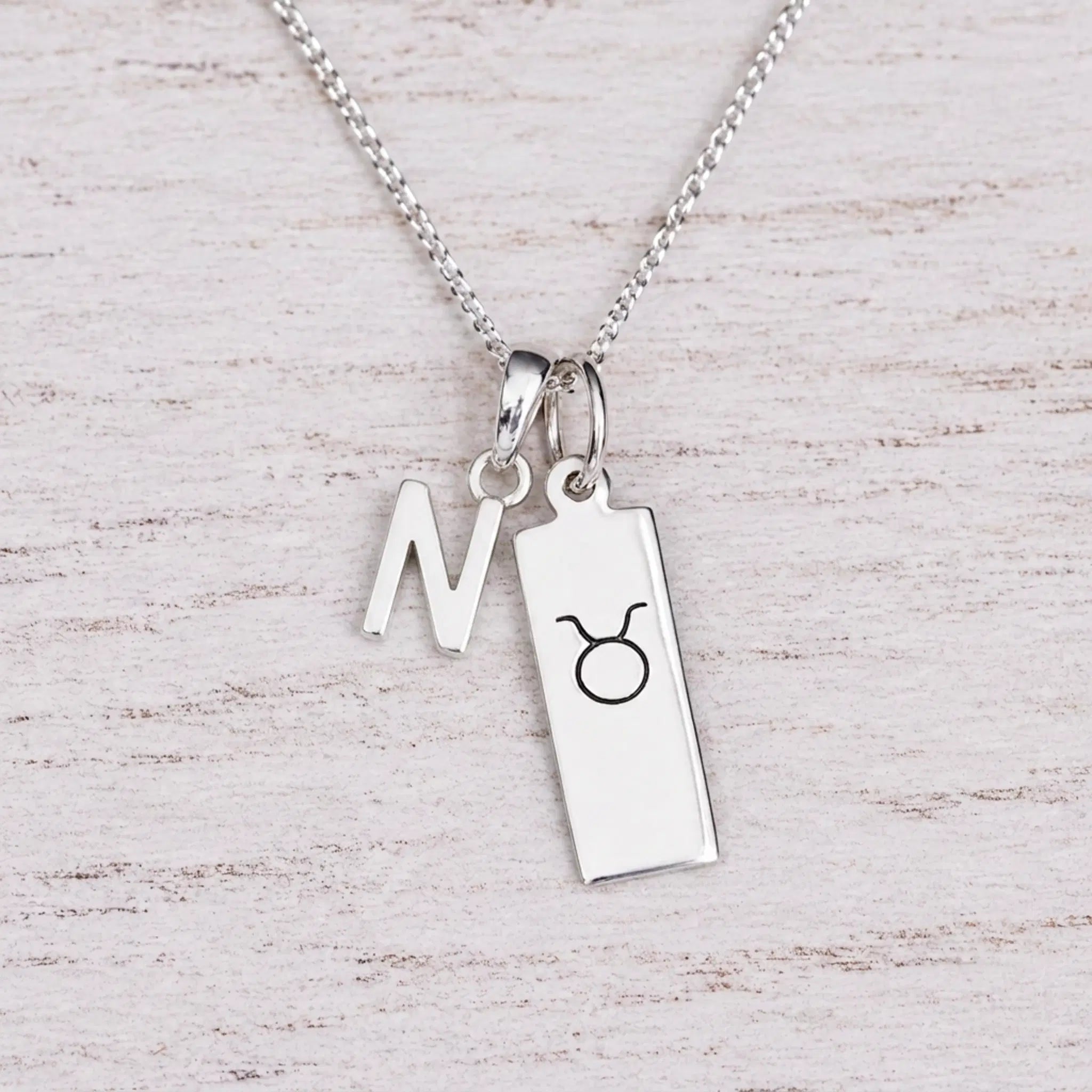Sterling silver N initial Pendant and Taurus Necklace on a fine silver chain on a light wooden background