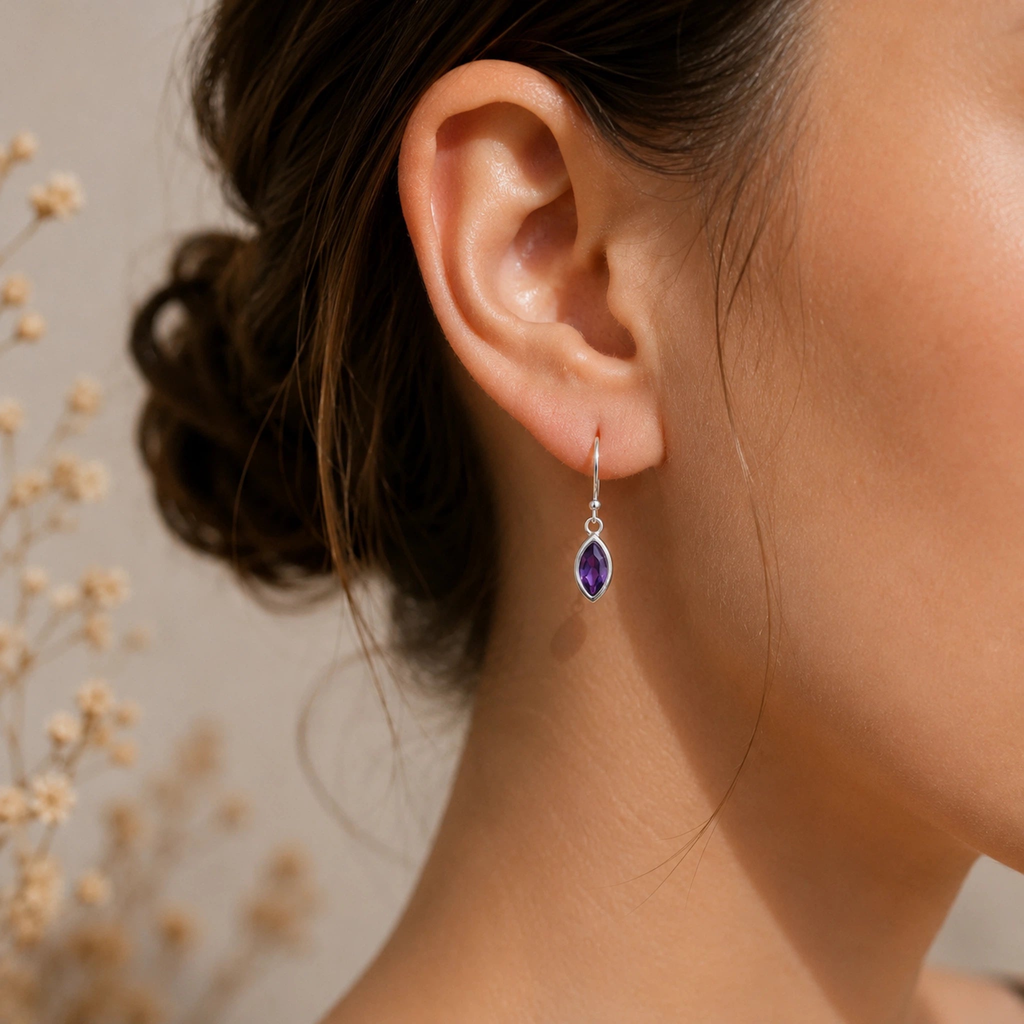 Close-up of an ear wearing a silver purple amethyst teardrop earring with a blurred background