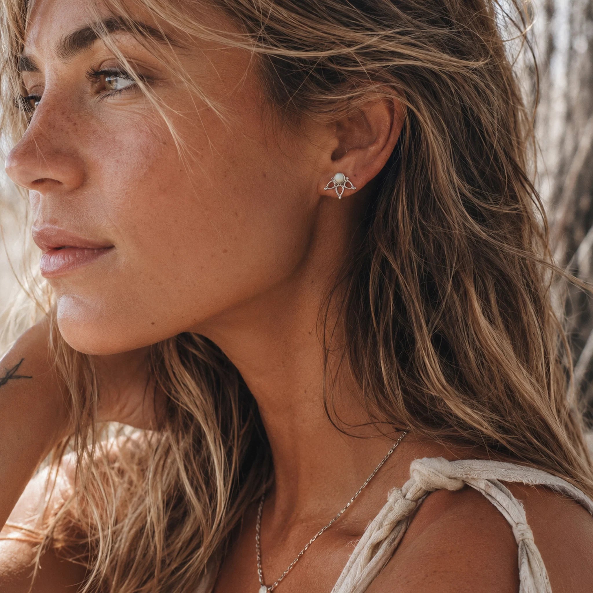 A close-up lifestyle shot of a woman with long light brown hair wearing a silver natural australian opal stud earrings and a delicate chain necklace.