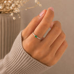 A close-up of a hand wearing a delicate silver ring with a small faceted natural emerald green gemstone, styled with a beige ribbed sweater sleeve against a soft neutral background.