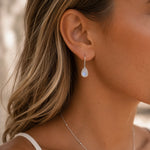 sterling silver moonstone earrings worn by a woman featuring teardrop natural faceted moonstones with french hook bezel set design