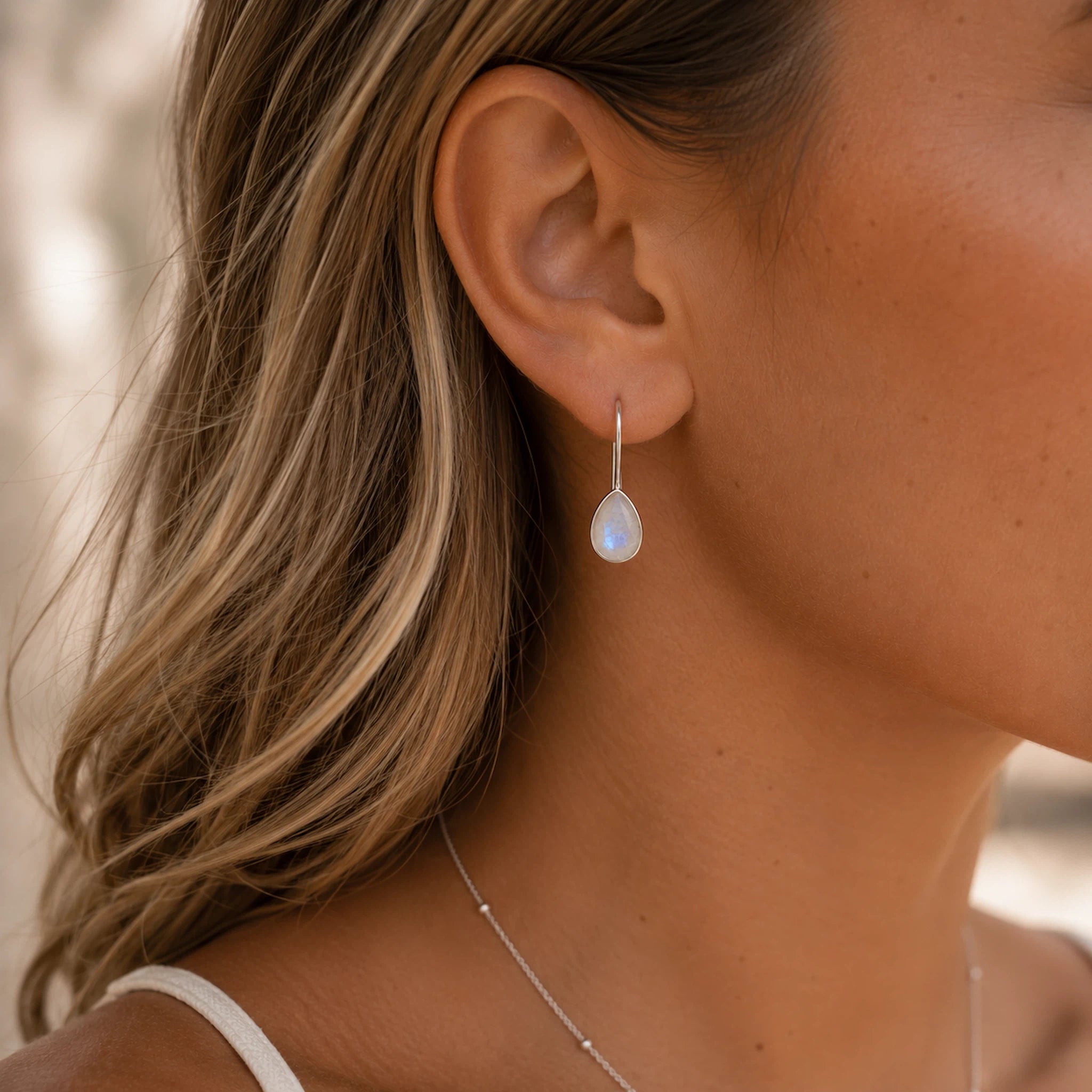 sterling silver moonstone earrings worn by a woman featuring teardrop natural faceted moonstones with french hook bezel set design