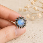 sterling silver sunrise ring with a round natural cabochon bezel set rainbow moonstone being held