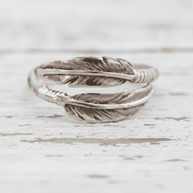 Silver feather-shaped ring on a light wooden surface