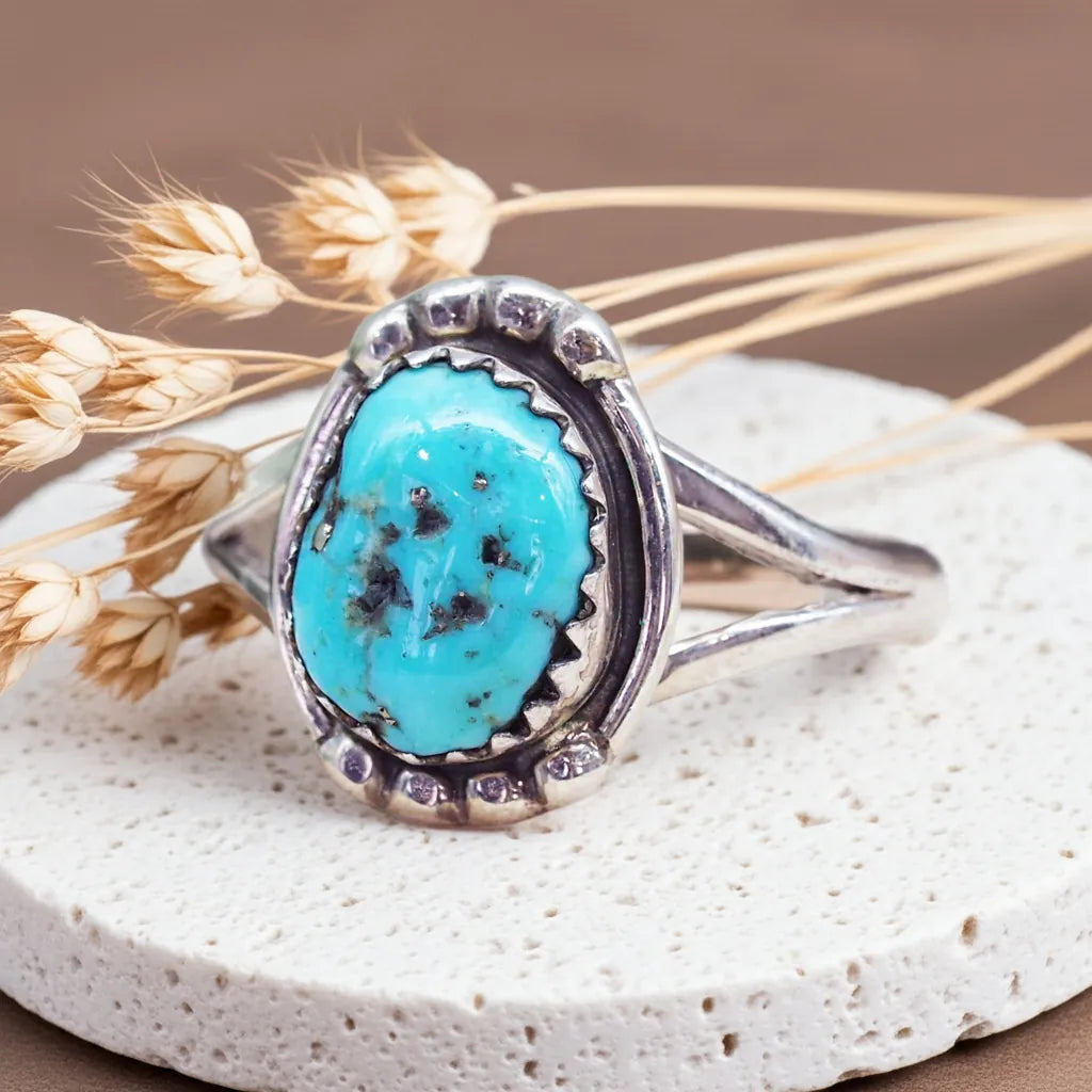 Silver ring with a turquoise stone on a stone surface with dried grass.