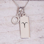 Sterling Silver O Initial pendant and Aries necklace on a fine silver chain on a light wooden background