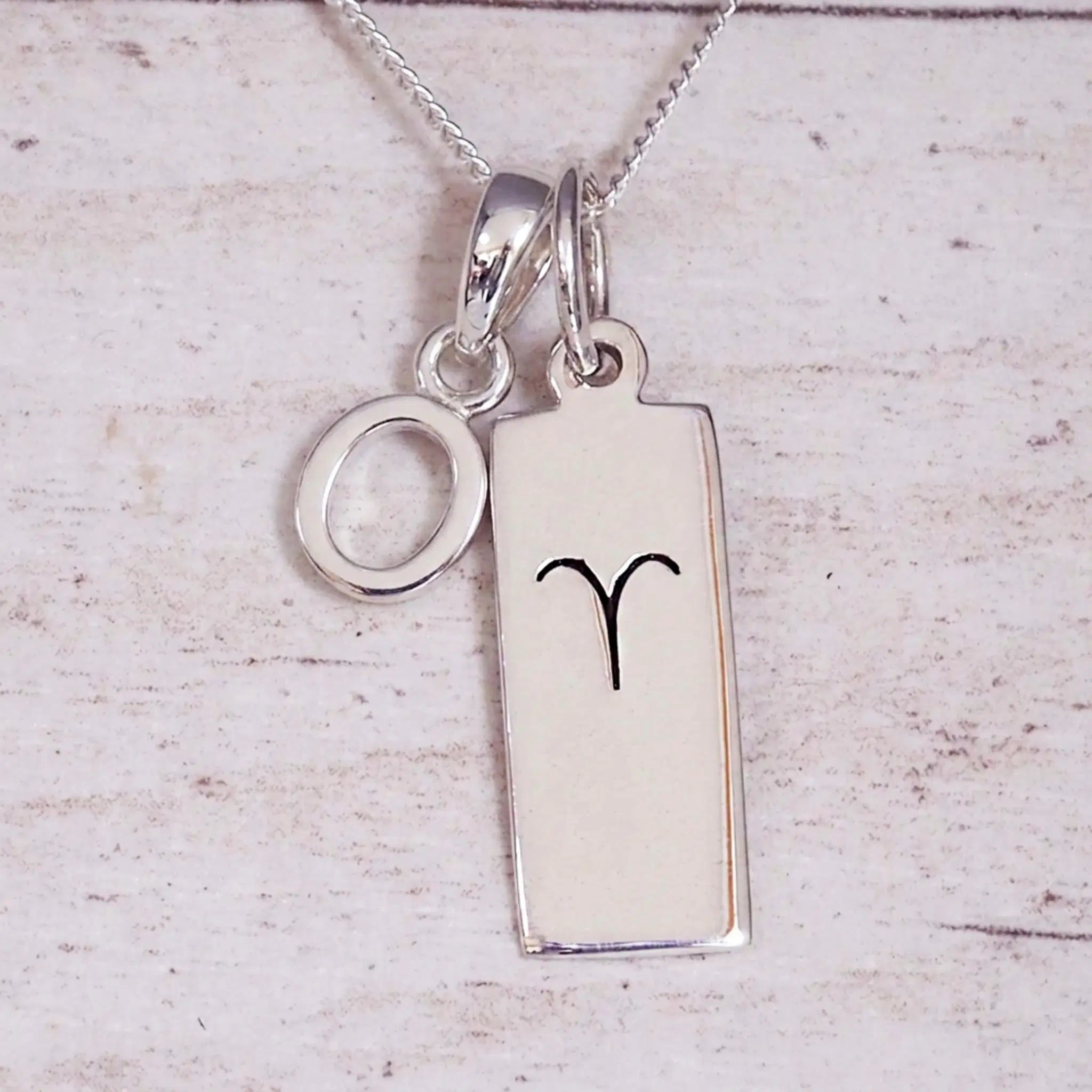 Sterling Silver O Initial pendant and Aries necklace on a fine silver chain on a light wooden background