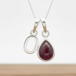 Silver initial o necklace with a teardrop-shaped red ruby gemstone pendant on a white background