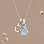Sterling silver initial O and November natural blue topaz necklace on a taupe background with sparse ivory flowers