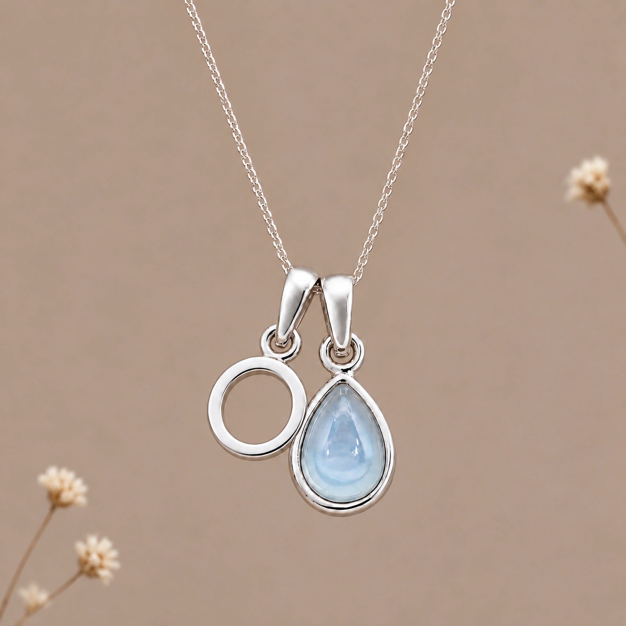 Sterling silver initial O and November natural blue topaz necklace on a taupe background with sparse ivory flowers