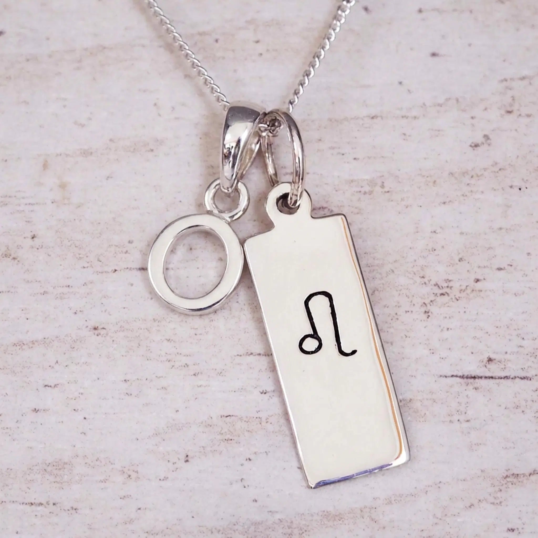 sterling silver initial o leo zodiac star sign pendant necklace against a light wooden background