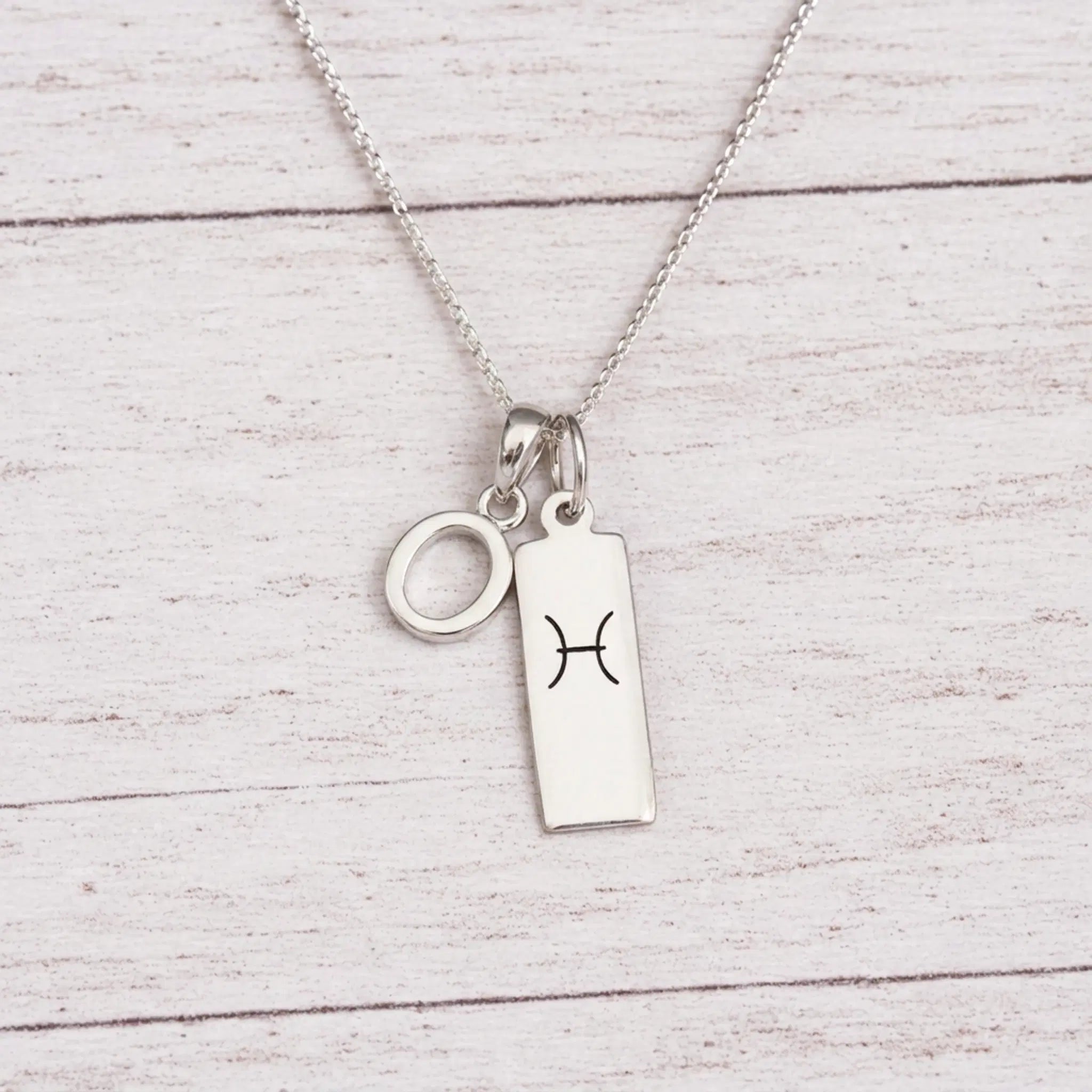 sterling silver O initial Pisces Necklace on a fine silver chain against a light wooden background