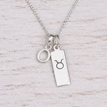Sterling silver O initial Pendant and Taurus Necklace on a fine silver chain on a light wooden background