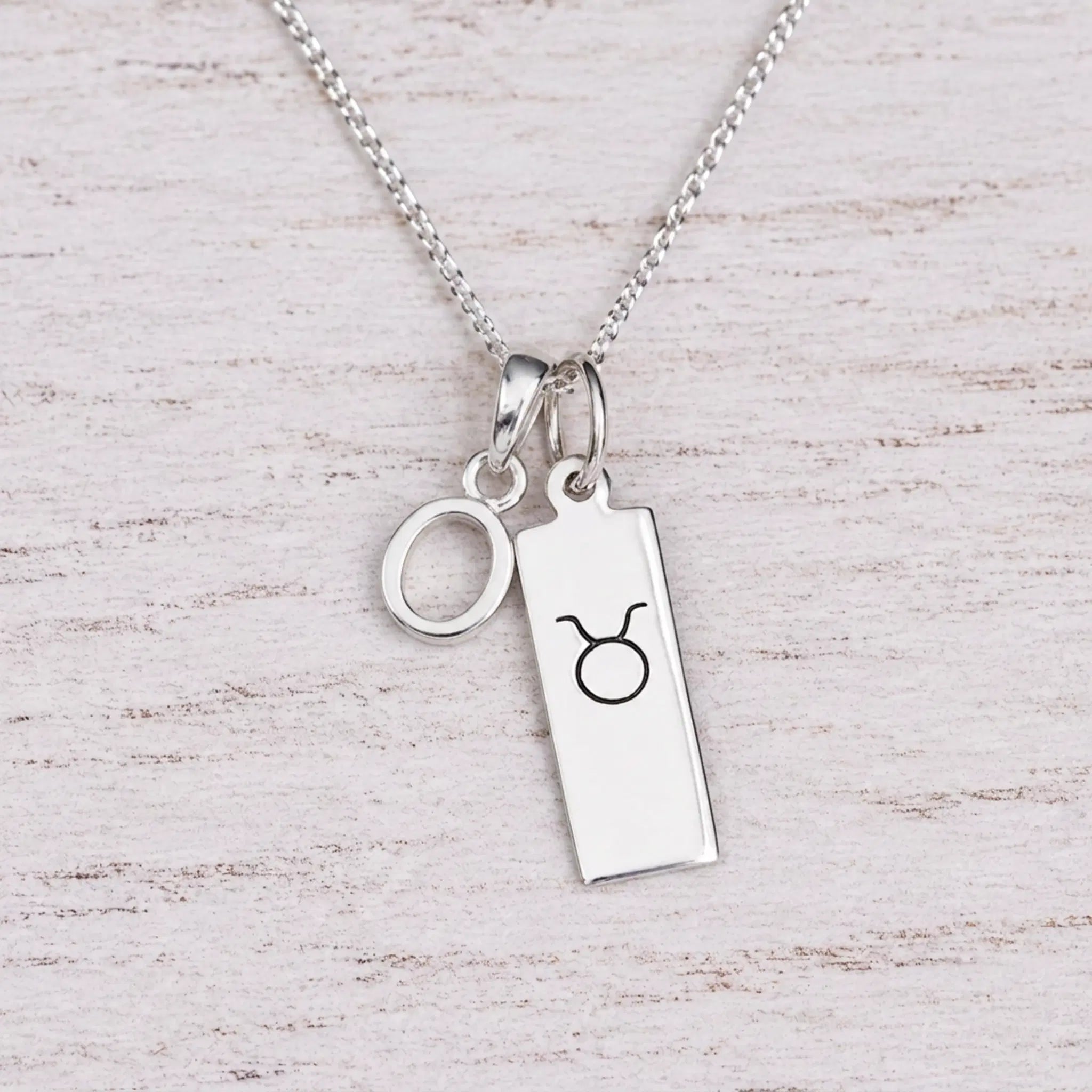 Sterling silver O initial Pendant and Taurus Necklace on a fine silver chain on a light wooden background