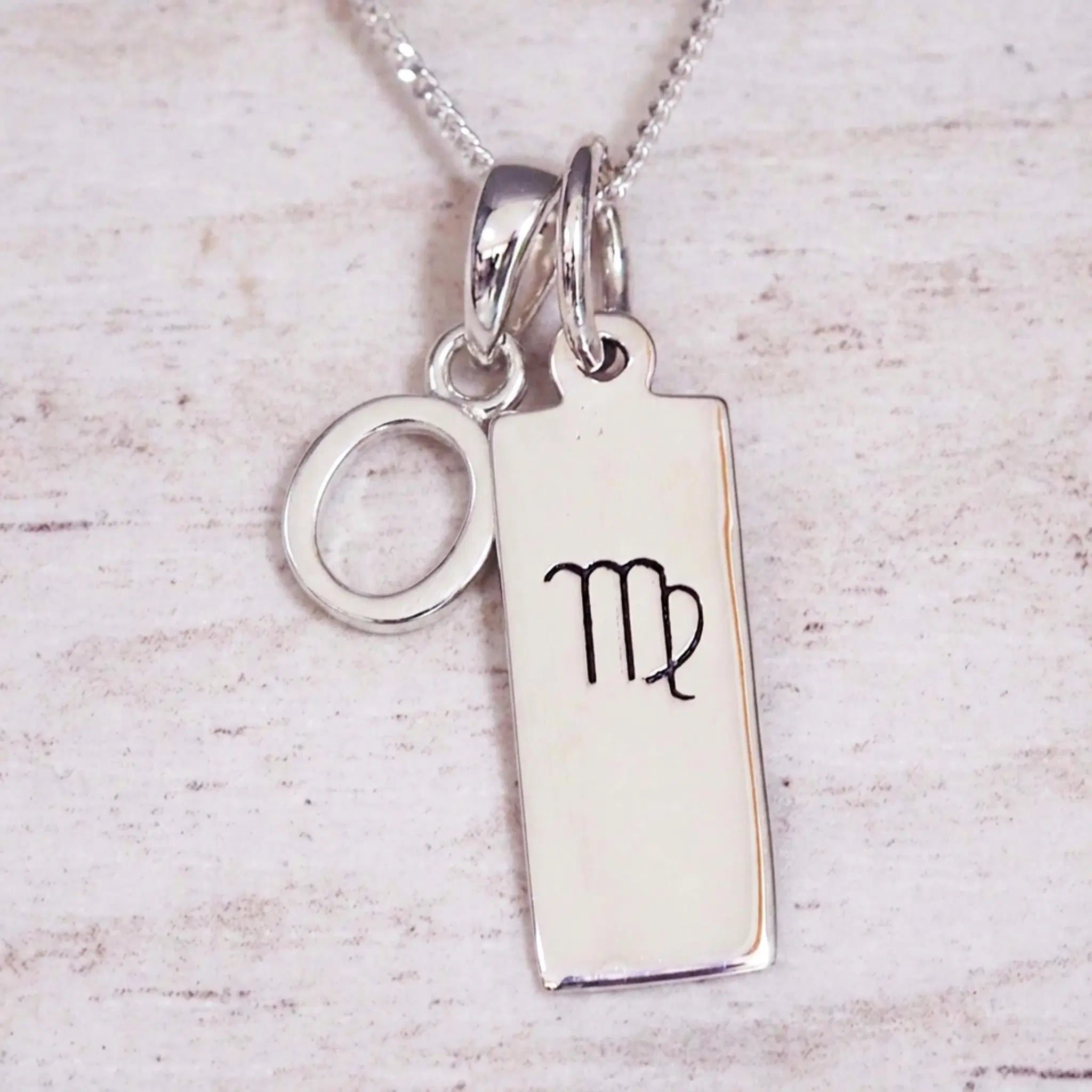 sterling silver initial o virgo zodiac star sign pendant necklace against a light wooden background