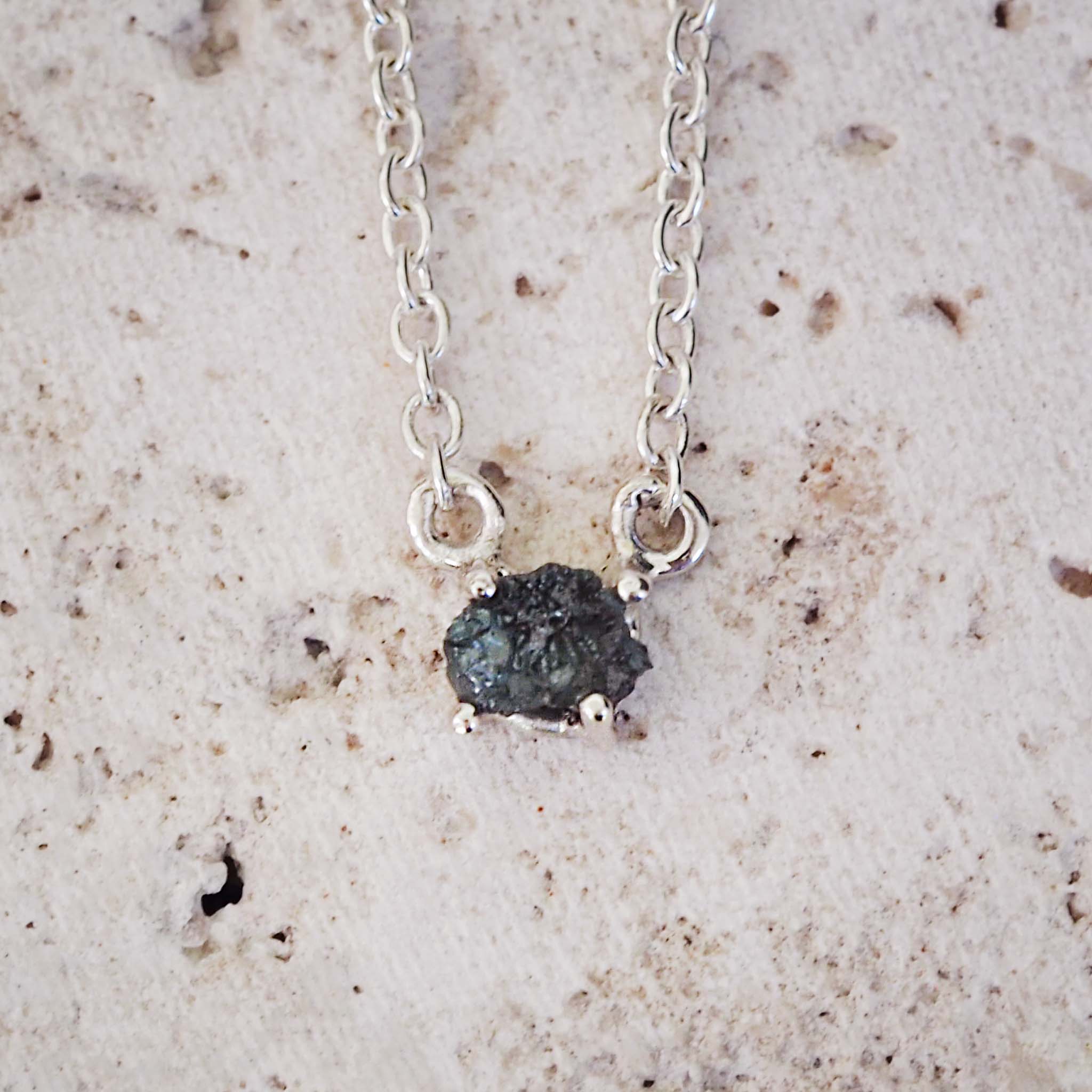Necklace with a dark green diamond stone pendant on a beige surface