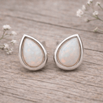 Teardrop-shaped opal earrings with silver setting on a light gray background