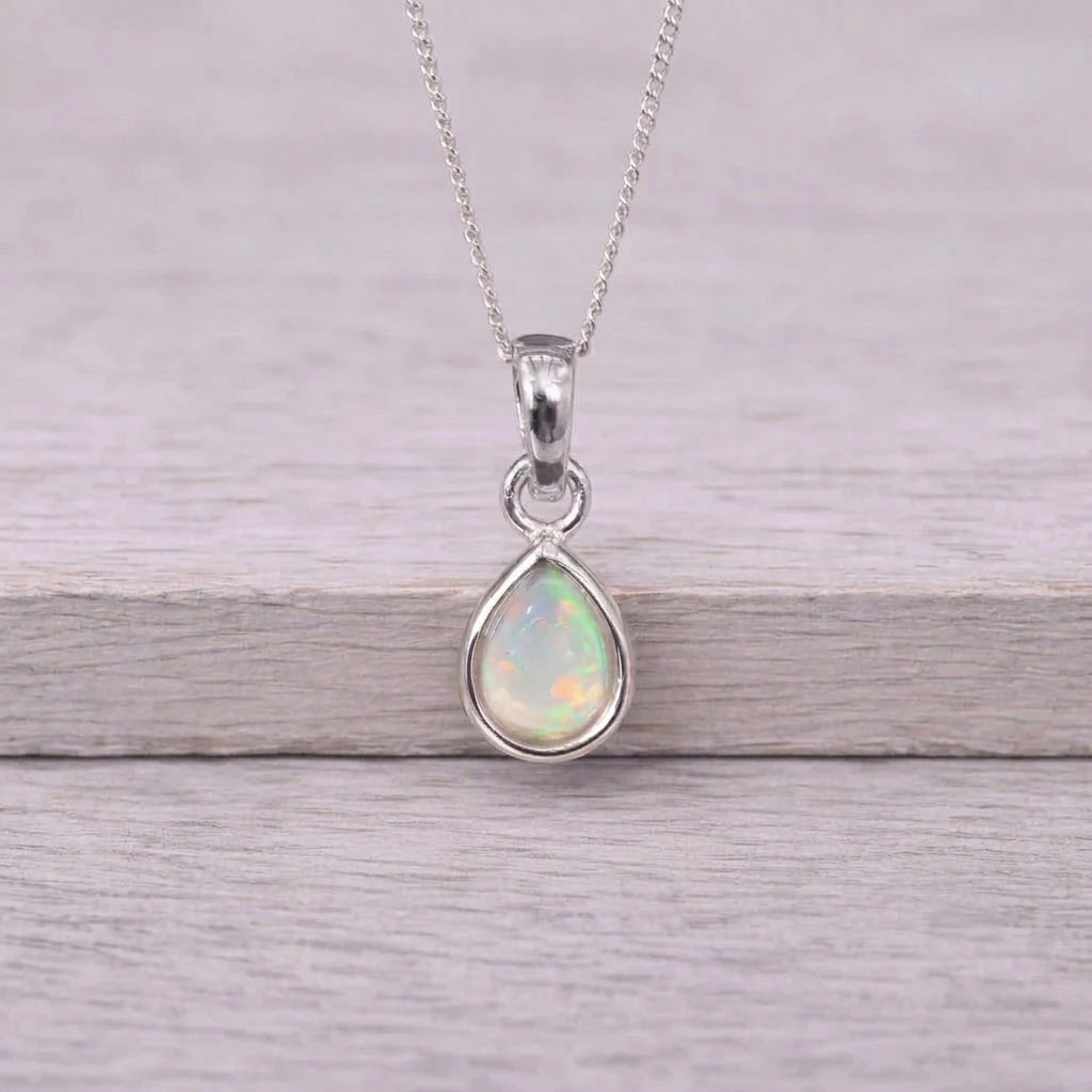 Silver October birthstone opal necklace on a wooden surface with flowers