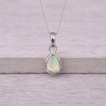 Silver October birthstone opal necklace on a wooden surface with flowers