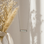 Necklace with a rectangular pendant hanging next to dried flowers on a neutral background