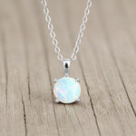 A sterling silver necklace with a round white opal pendant, resting on a light brown wooden surface.