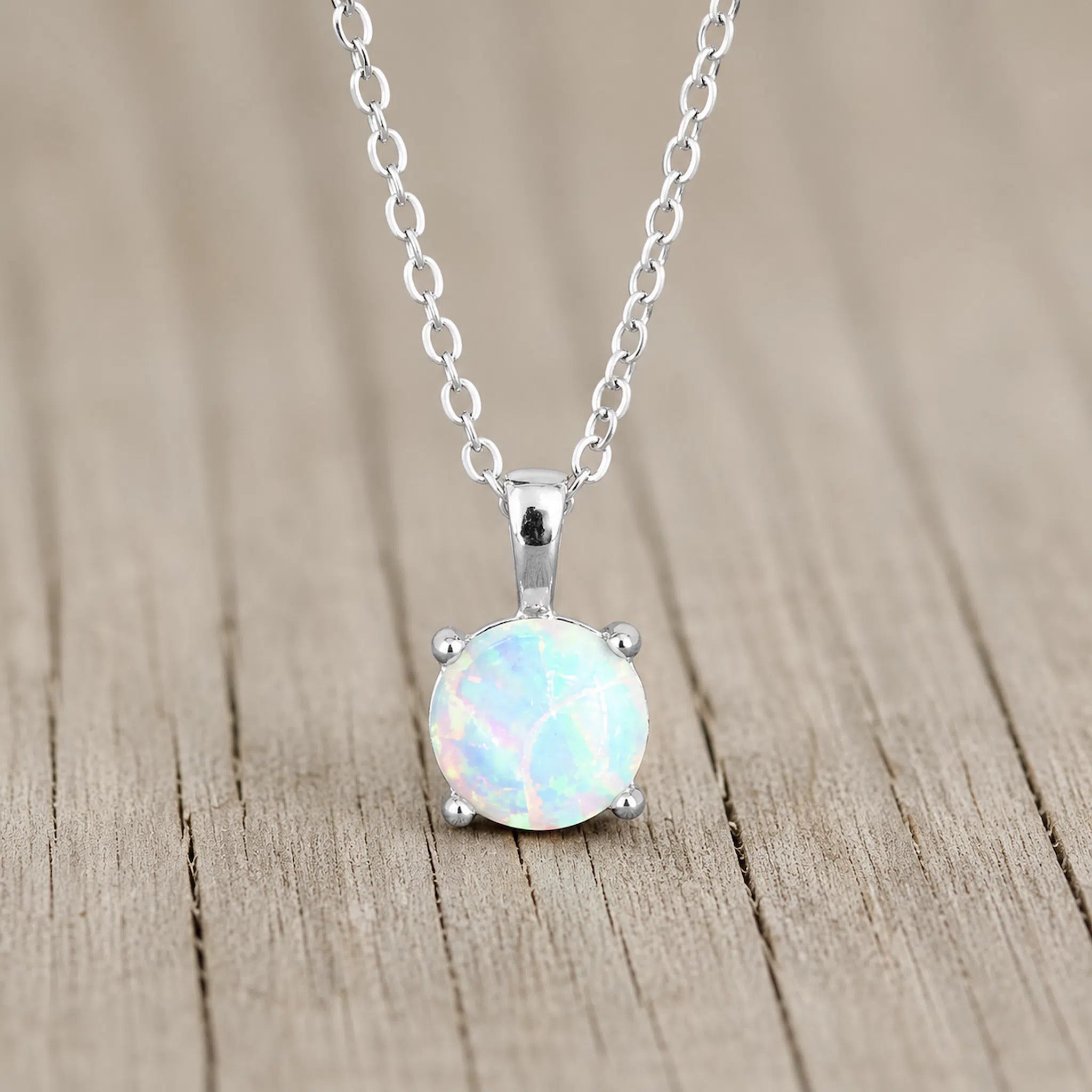 A sterling silver necklace with a round white opal pendant, resting on a light brown wooden surface.