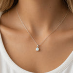 A delicate silver chain necklace with a small white opal pendant, shown worn on a model's neck over a white ribbed top.