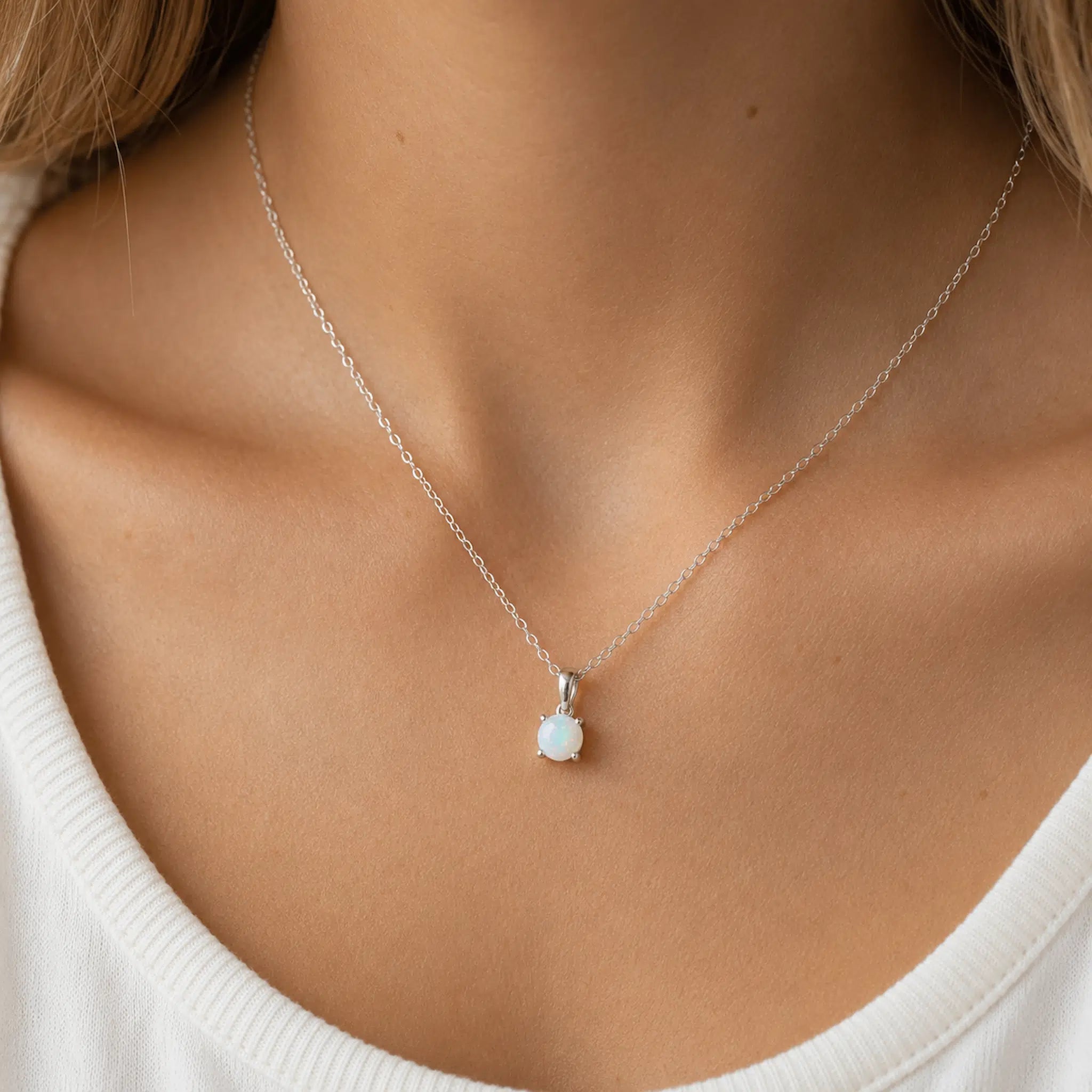 A delicate silver chain necklace with a small white opal pendant, shown worn on a model's neck over a white ribbed top.
