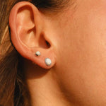 Close-up of an ear wearing two silver white opal earrings with a blurred background