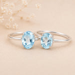 sterling silver rings with a oval shaped faceted claw set blue topaz gemstones on a light surface.