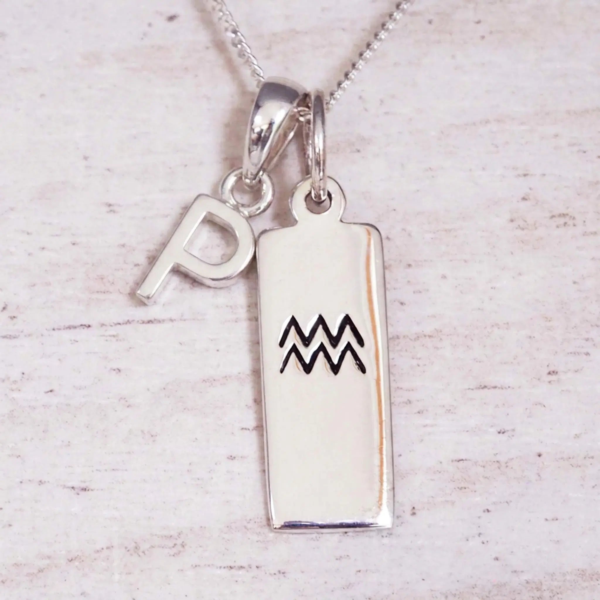 Sterling Silver P Initial and Aquarius Necklace on a fine silver chain against a light wooden background