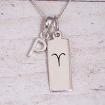 Sterling Silver P Initial pendant and Aries necklace on a fine silver chain on a light wooden background
