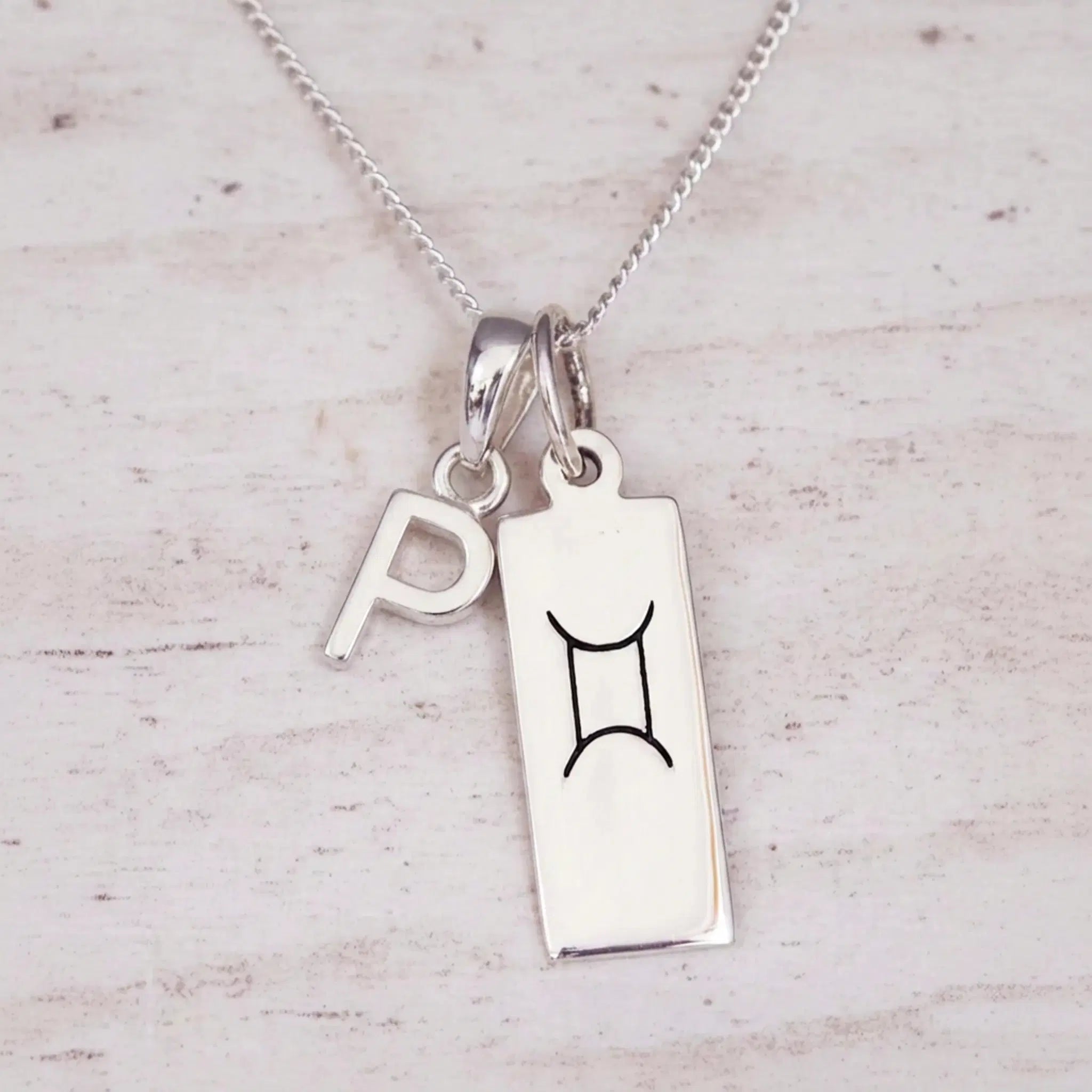 Sterling silver P initial and GeminI Necklace on a fine silver chain on a light wooden background