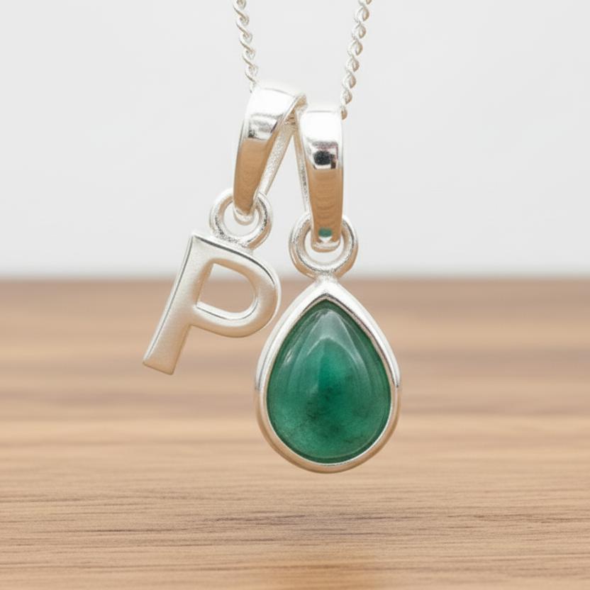 Silver Initial P necklace with a teardrop-shaped Emerald gemstone pendant hanging above a rustic wooden surface