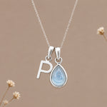 Sterling silver initial P and November natural blue topaz necklace on a taupe background with sparse ivory flowers