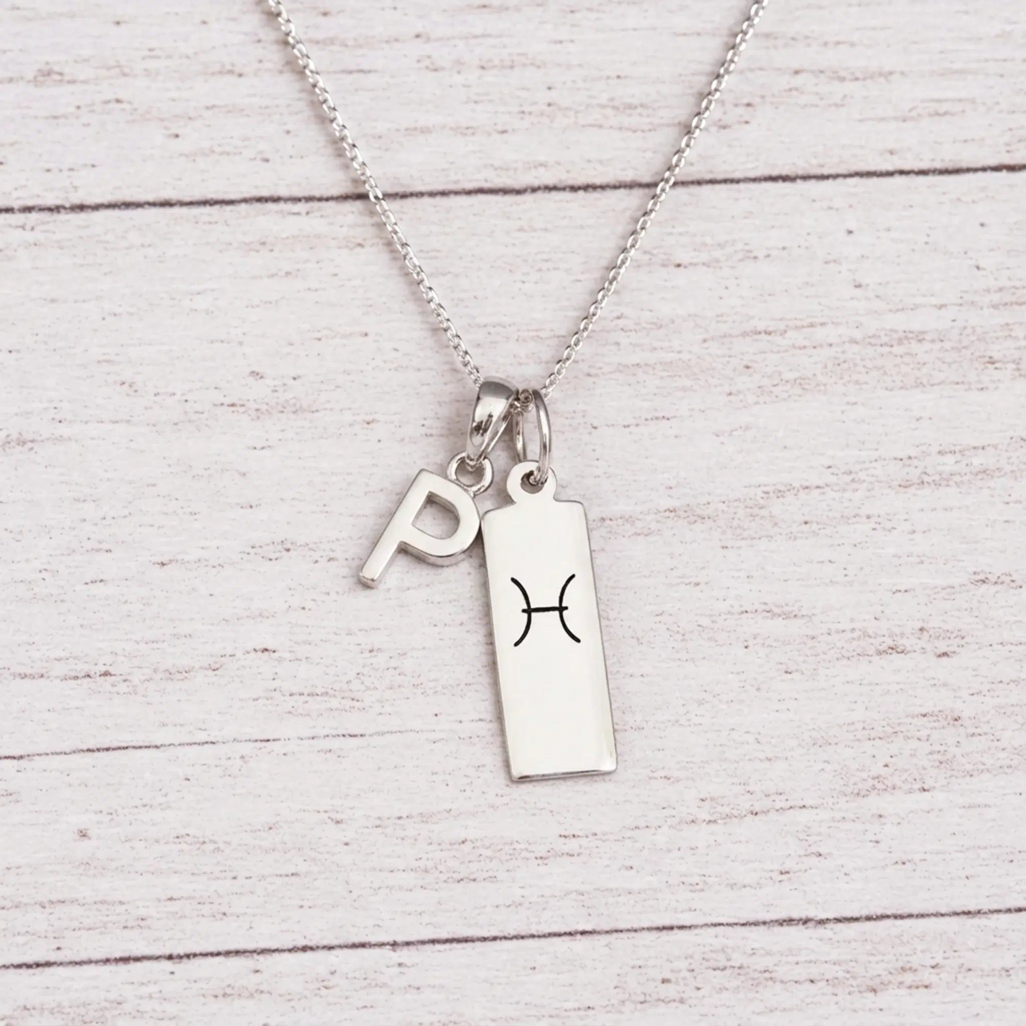 sterling silver P initial Pisces Necklace on a fine silver chain against a light wooden background