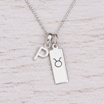 Sterling silver P initial Pendant and Taurus Necklace on a fine silver chain on a light wooden background