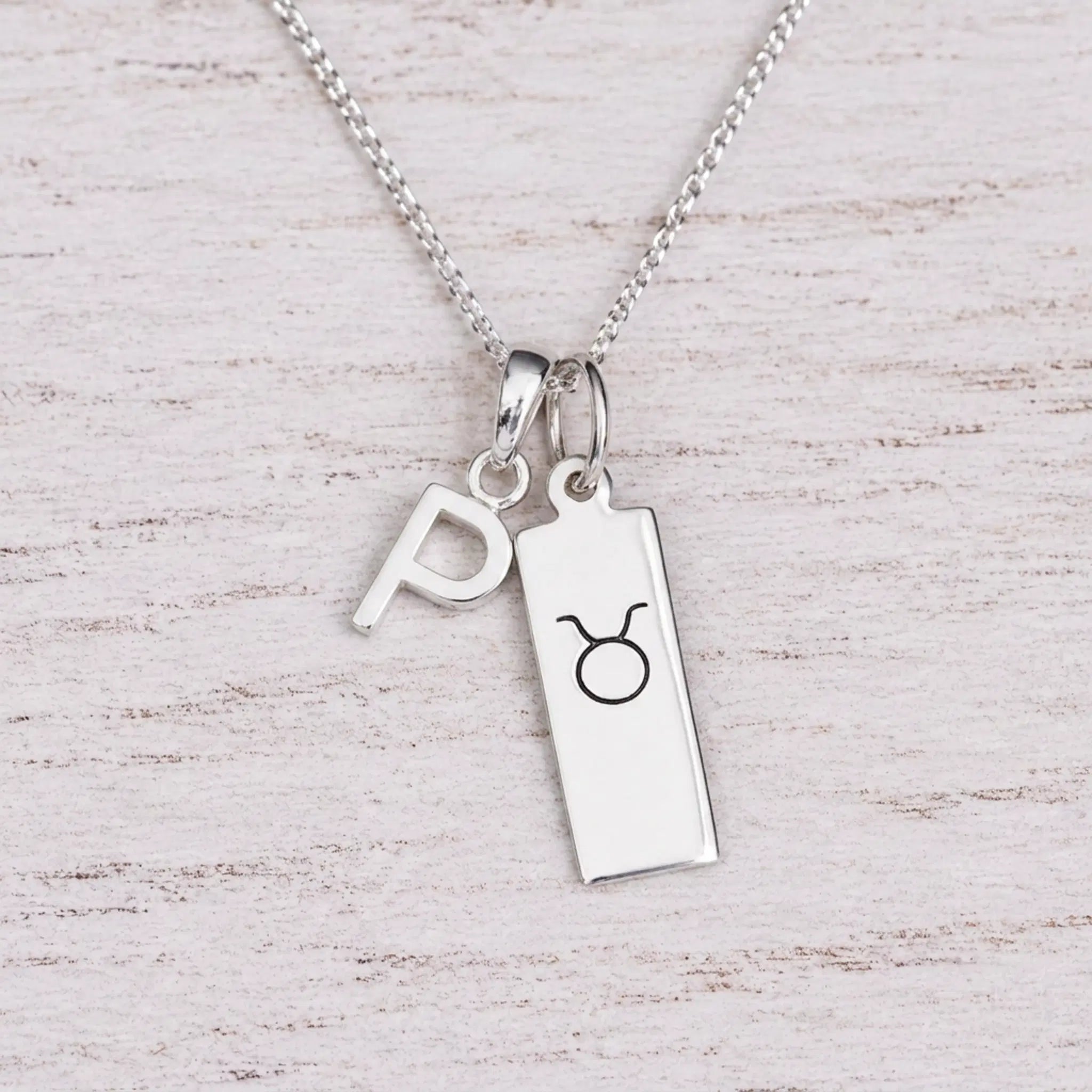 Sterling silver P initial Pendant and Taurus Necklace on a fine silver chain on a light wooden background