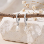 Silver pearl and CZ huggie earrings, a pair hanging from a natural twig